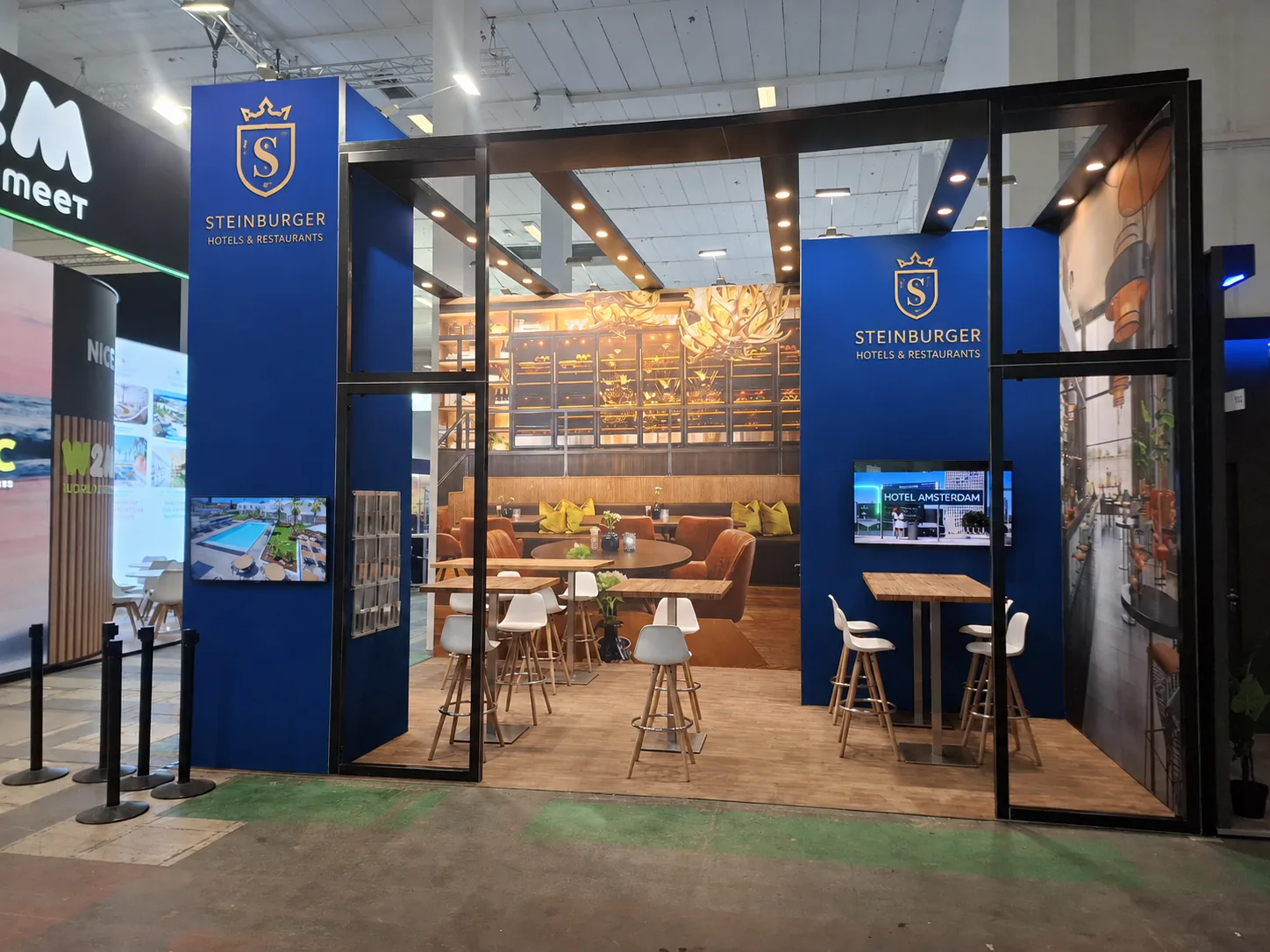 Custom hotel group exhibition stand with a perimeter steel frame, timber floor, bar stools and wall-mounted screen