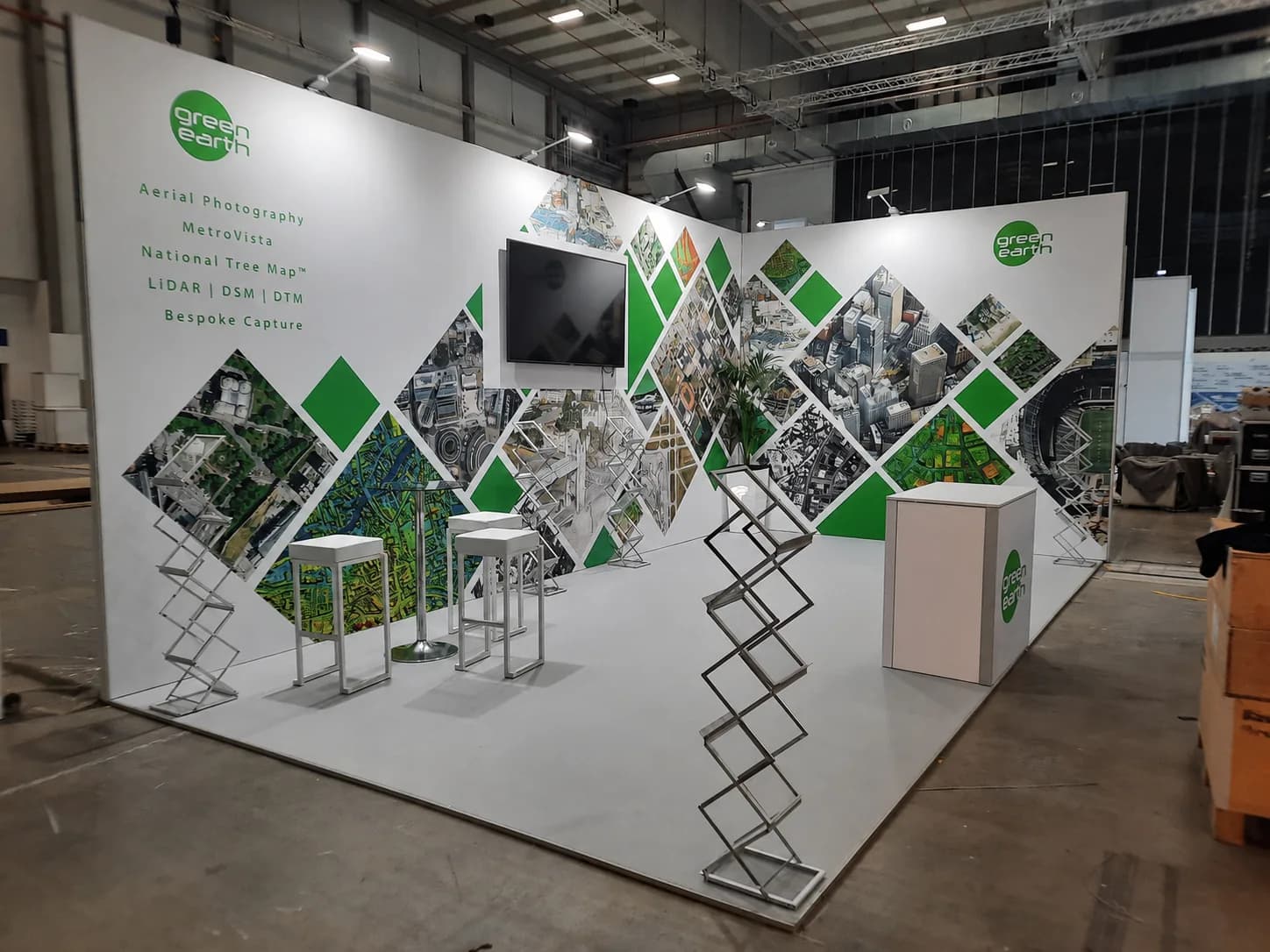 Modular exhibition stand with a white diamond-pattern graphics wall, wall-mounted screen and poseur tables