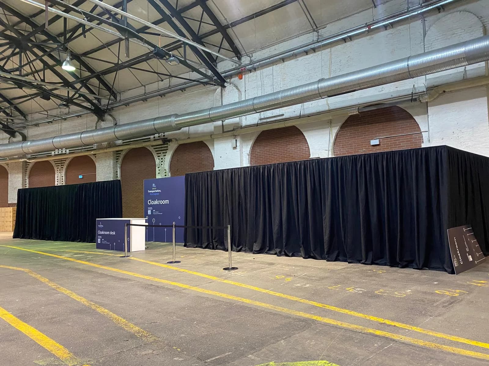 Pipe-and-drape installation with black fabric forming a cloakroom area in an event hall